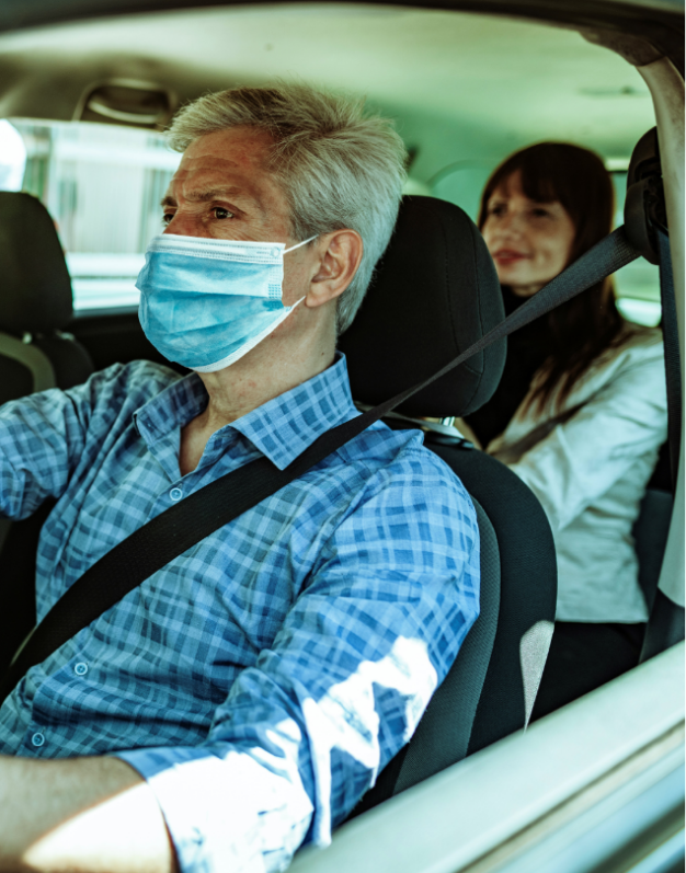 A man wearing a mask drives a businesswoman in a car. The image serves to promote carpooling as means of a safer return to work.